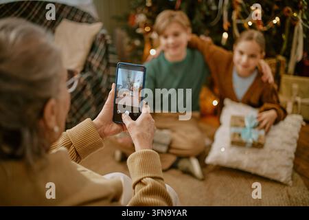 Senior Woman Photographing Grandchildren with Smartphone on Christmas Stock Photo