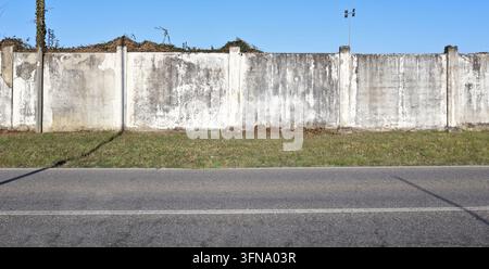 Weathered white plaster surrounding wall with grass and road in front. Grunge background for copy space. Stock Photo
