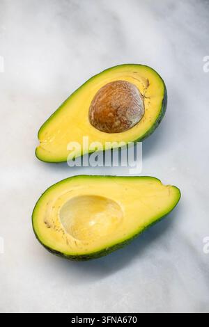 Vertical Shot of Fresh Ripe Avocado Halves with Seed Pit on White Marble Background Stock Photo