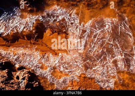 A close-up view of delicate ice crystal patterns formed on reddish mud puddles during a freezing day in Alhambra, Ciudad Real. Stock Photo
