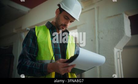Thoughtful Caucasian builder man writing notes at construction site male in hardhat uniform planning project foreman developing structure contractor Stock Photo