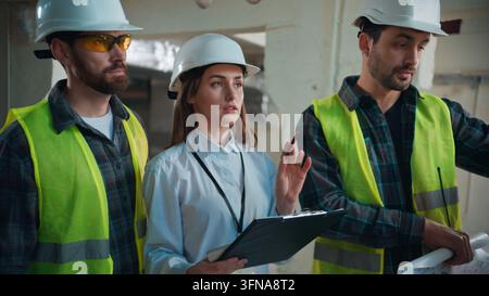 Caucasian men discussing blueprint with female inspector at construction site males negotiating woman contractor tasks using radio colleagues Stock Photo