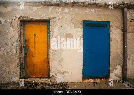 View of a weathered wall featuring a vibrant yellow door and a contrasting blue door in Bari, Apulia, Italy. Stock Photo
