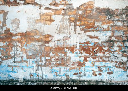 Textured surface of a vintage brick wall showing cracked plaster and flaking paint layers. Concept of urban decay, architectural weathering, rustic te Stock Photo