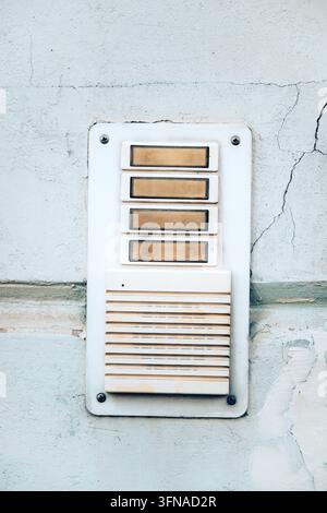 Vertical close-up of a vintage white intercom panel with push buttons mounted on a cracked stucco wall. Stock Photo