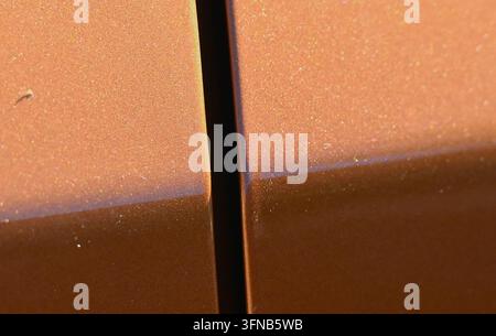detailed photograph of a textured copper-orange painted metal surface featuring a dark vertical panel seam line and soft lighting. Stock Photo