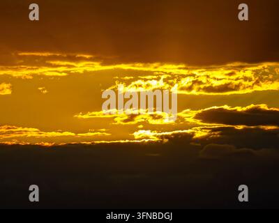 Intense golden sunset sky with dramatic dark cloud layers and glowing light streaks with copy space Stock Photo