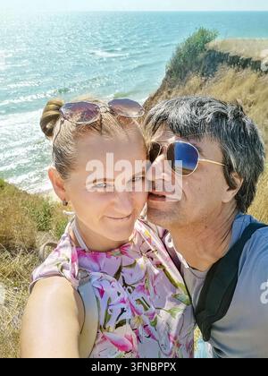 Happy romantic couple taking selfie on cliff edge over Black Sea in Odesa region, Ukraine. Summer vacation, love and lifestyle travel concept Stock Photo