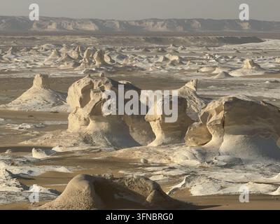 Large chalk sculptures rising from a vast white plain, photographed at White Desert National Park in Egypt's Western Desert. Stock Photo