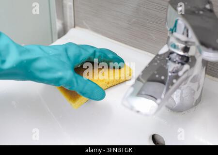 Hand cleaning bathroom sink and chrome faucet with sponge. Household background for bathroom cleaning hygiene sanitation chores and home care. Stock Photo