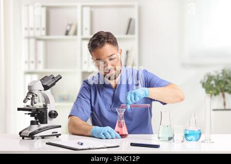Young male scientist pouring liquid from a test tube into a flask in a laboratory Stock Photo