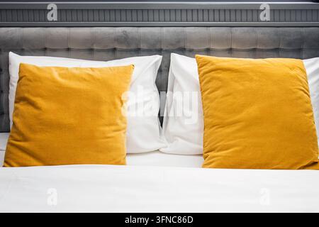 Two mustard yellow velvet cushions on white pillows and bedding against a gray tufted upholstered headboard. Stock Photo