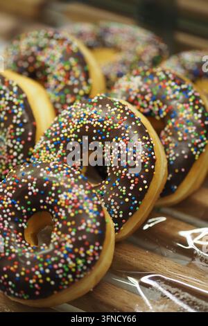 Donuts with chocolate glaze and colorful sprinkles on display at a bakery Stock Photo