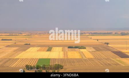 Aerial view of agricultural farmland under dramatic dark storm clouds. Rural landscape with village, green and golden fields Stock Photo