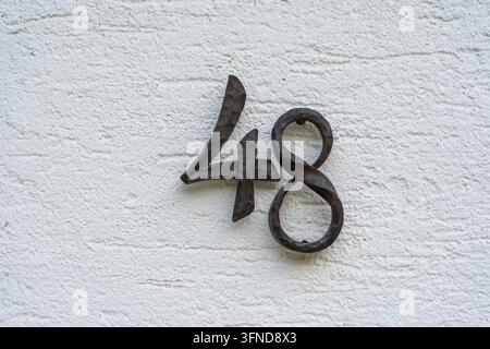 Metal house number 48 on a white stucco wall background, close up Stock Photo