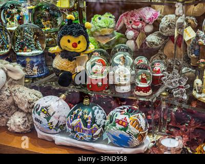 Christmas snow globes, painted glass ornaments and plush animal toys displayed in a souvenir shop, featuring miniature Santa Claus figures and winter Stock Photo