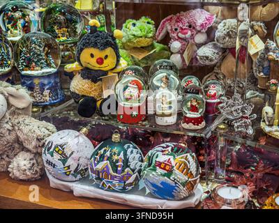 Christmas snow globes, painted glass ornaments and plush animal toys displayed in a souvenir shop, featuring miniature Santa Claus figures and winter Stock Photo