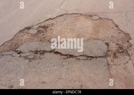 A pothole and cracks on an asphalt road surface. Infrastructure failure, municipal maintenance problems, and street repair needs Stock Photo