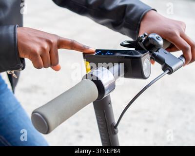 Detail shot of a young African woman switching on the digital dashboard of an electric scooter on a city street Stock Photo