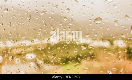 Close up of raindrops on window glass pane with warm blurry outdoor background creating cozy atmospheric autumn mood for design and backdrop. Stock Photo