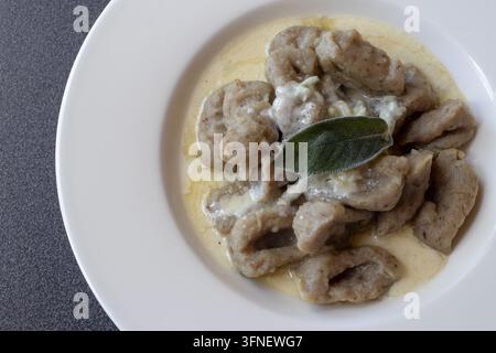 Top view of grey semolina gnocchi in a creamy gorgonzola sauce topped with a fresh sage leaf on a white plate, dark speckled counter Stock Photo
