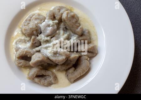 Top view of grey semolina gnocchi in a creamy gorgonzola sauce with a dollop of blue cheese cream on a white wide rim plate, dark counter edge Stock Photo