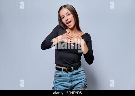 Touched young woman holding hands on chest in studio portrait Stock Photo