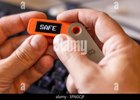 hardware Bitcoin wallet held in white hands with message SAFE on screen. Closeup with selective focus. Stock Photo