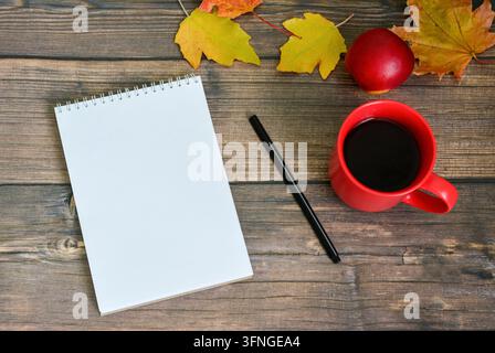 Red Notebook with black pen and Coffee Mug on Wooden Table with Autumn Leaves Stock Photo