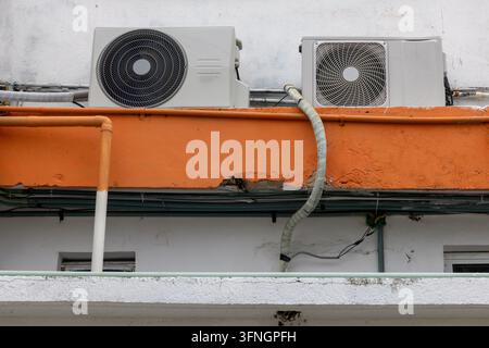 Two Air Conditioning Outdoor Units Mounted on Weathered Building Wall with Pipes and Cables – Urban HVAC Installation Stock Photo