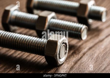 Close up view of metal bolts and nuts arranged on a brown wooden surface Stock Photo