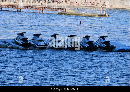 photograph showing a row of personal watercraft jet skis lined up on a floating dock in the blue sea under bright daylight Stock Photo