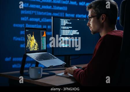 Developer sits in a dimly lit workspace, in front screens displaying code and data science data graph. Focused programmer working, deeply immersed in solving an artificial intelligence problem Stock Photo