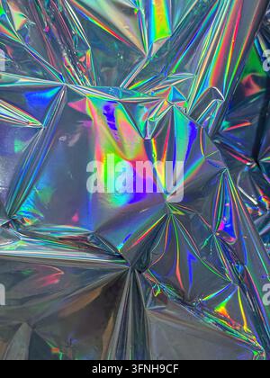 Abstract background featuring crumpled iridescent foil with vibrant rainbow colors and sharp reflections. Shiny metallic surface creates a futuristic Stock Photo