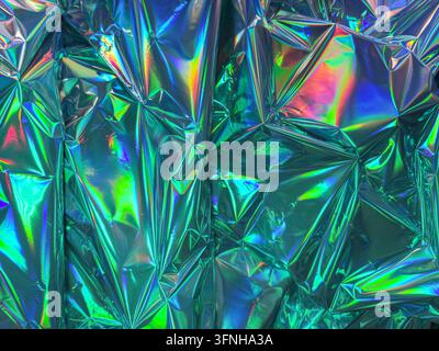 Close up of crinkled metallic foil material with vibrant iridescent colors and sharp geometric folds. Reflective surface creates rainbow highlights an Stock Photo