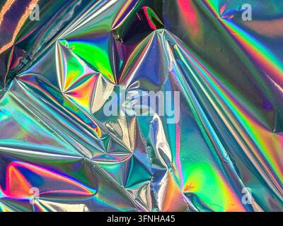Abstract colorful texture featuring iridescent crumpled foil with rainbow spectrum highlights. Reflective surface catches light, creating dynamic patt Stock Photo