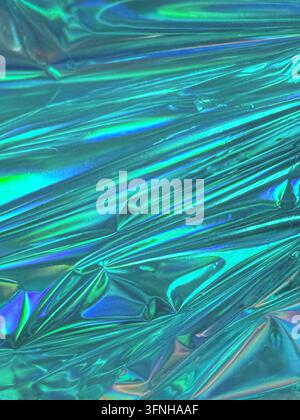 Abstract shimmering surface with iridescent teal and blue hues. Wrinkled metallic texture reflects light creating vibrant colorful patterns. Minimalis Stock Photo