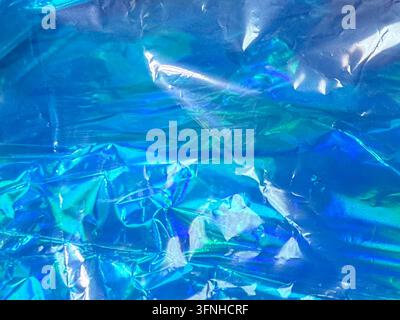 Abstract background featuring crumpled blue holographic material, with iridescent sheen reflecting light. Deep blues and turquoise hues dominate. Stock Photo