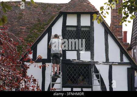 A painter on a ladder works the black timber of a white historic house in Rye.Rye, England Stock Photo