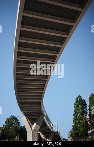 Low-angle view of a curved modern concrete bridge spanning an urban street in Porto, Portugal, with structural beams, support columns, trees, and clea Stock Photo