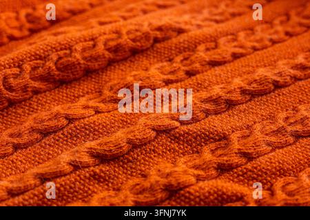 Close-up macro view of orange cable knit sweater fabric, showing raised braided stitches and soft wool texture. Warm autumn textile background with de Stock Photo