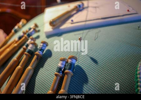 High angle view of a senior woman working on bobbin lace, handling wooden bobbins on a cushion with a pin cushion and pattern chart nearby. Stock Photo