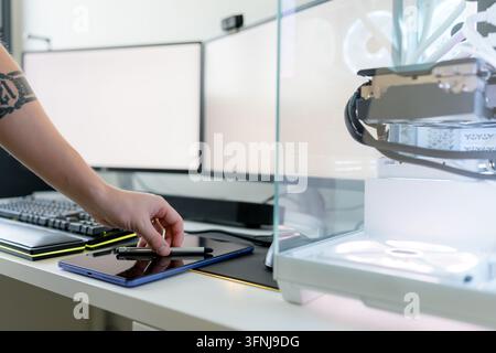 Close-up of a young man using an AI tool beside a gaming computer, keyboard and smartphone in a modern workspace with robotic equipment and digital te Stock Photo