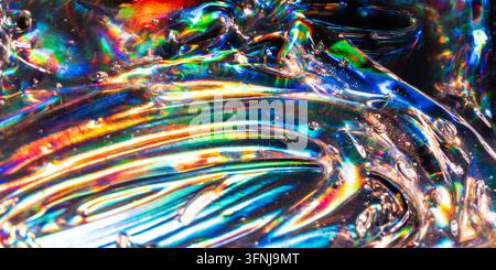 Macro view of iridescent liquid glass with vivid rainbow reflections, rippling curves, and glossy transparent surfaces forming a vibrant abstract back Stock Photo