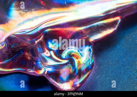 Close-up of crumpled metallic foil with iridescent reflections in cyan, magenta, red, and gold, creating a vivid abstract background with glossy folds Stock Photo
