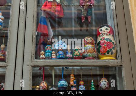 A shop window displays Russian matryoshka nesting dolls, traditional costume figurines, and painted ornaments on wooden shelves in Helsinki, Finland Stock Photo