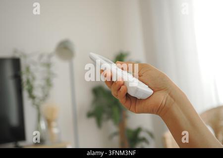 A person is using a air condition remote control while sitting in a living room Stock Photo