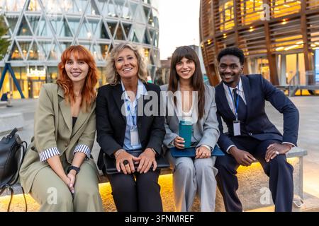 Diverse group of business professionals smiling outdoors in an urban setting, showcasing teamwork, partnership and corporate success with modern citys Stock Photo