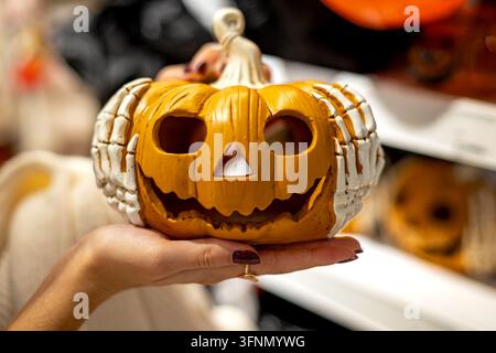 Halloween jack o lantern decoration with skeleton hands, smiling pumpkin ornament held in a woman's hands at an autumn seasonal market. Stock Photo