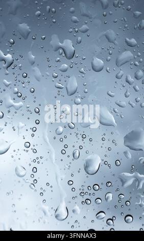Macro view of multiple rain drops and moisture patterns on a window glass with soft grey daylight filtering through Stock Photo